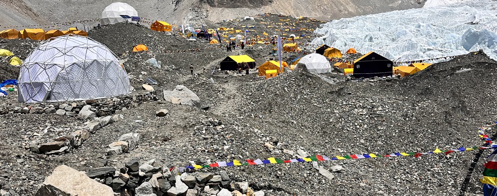 Yellow and white expedition tents pitched on the rocky moraine of the Khumbu Glacier at Mount Everest Base Camp.